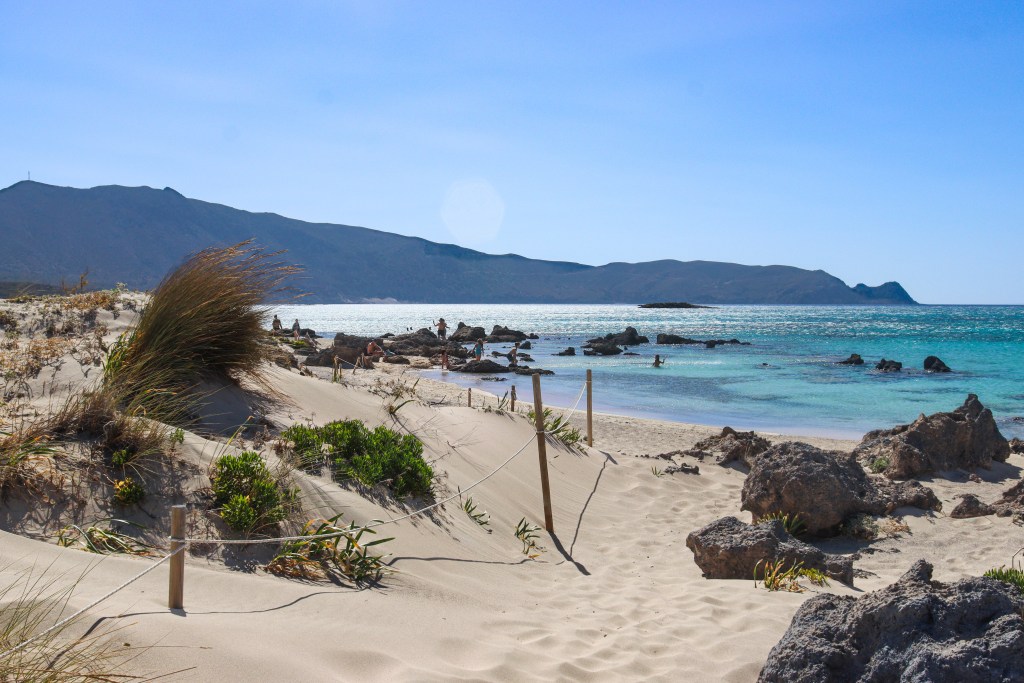 Elafonisi – Your Travel Guide to Crete’s Famous Pink Beach Sand dunes and rocks at Elafonisi Beach with mountain views