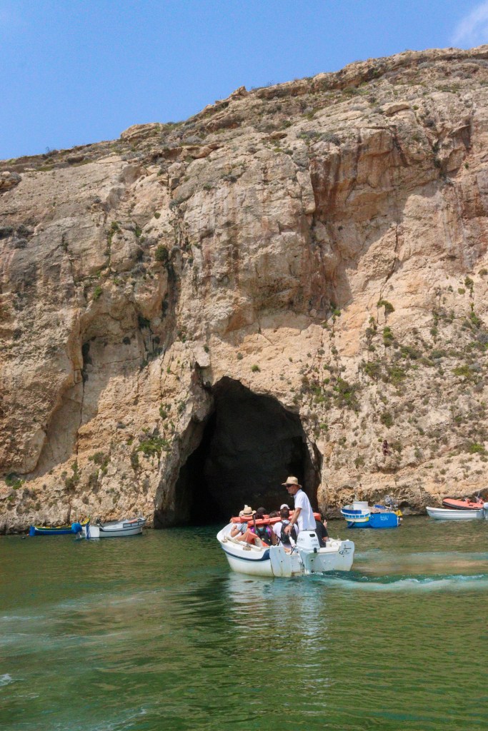 Mała łódź z turystami wypływa z malowniczej zatoki Inland Sea na Gozo przez skalny tunel prowadzący w kierunku Morza Śródziemnego