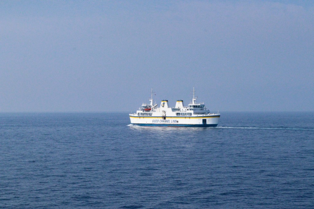 Ferry branco e azul da Gozo Channel Line a navegar em pleno mar entre Malta e Gozo sob céu claro