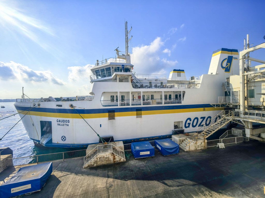 Ferry Gaudos da Gozo Channel atracado no porto, com céu azul e sol brilhante, pronto para viajar entre Malta e Gozo
