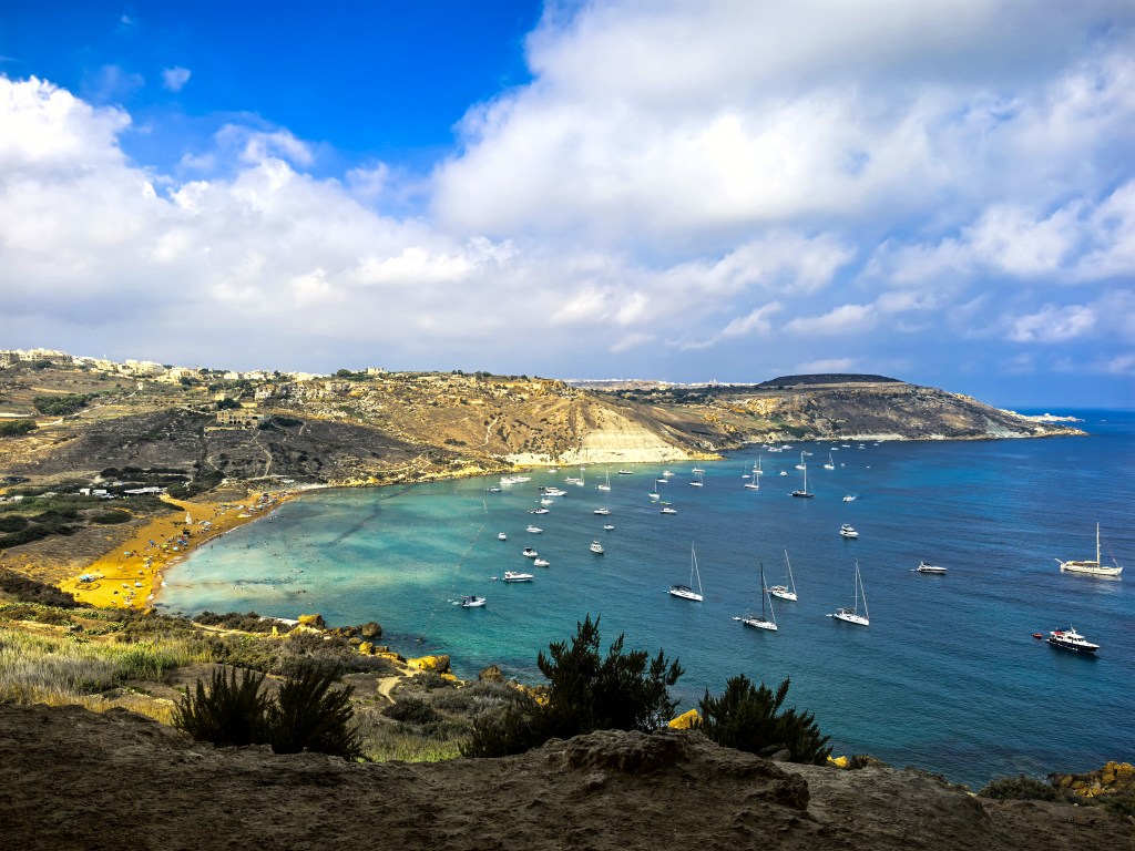 Paisagem costeira da Baía de Ramla vista da entrada da gruta Tal-Mixta, com mar azul, praia e colinas de Gozo