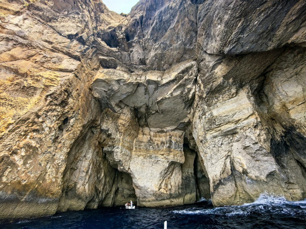 Pequeno barco a navegar em direção à monumental entrada da gruta, rodeada de penhascos, no Inland Sea de Gozo
