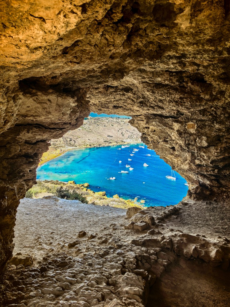 Vista panorâmica do interior rochoso da gruta Tal-Mixta com a Baía de Ramla e o mar azul de Gozo ao fundo