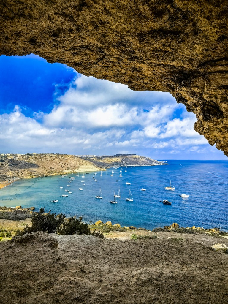 Exploring Gozo in One Day – What to See Iconic view of Ramla Bay from inside Tal-Mixta Cave on Gozo, Malta, with turquoise water, golden beach, and sailing boats – a must-see landscape for a Gozo itinerary.