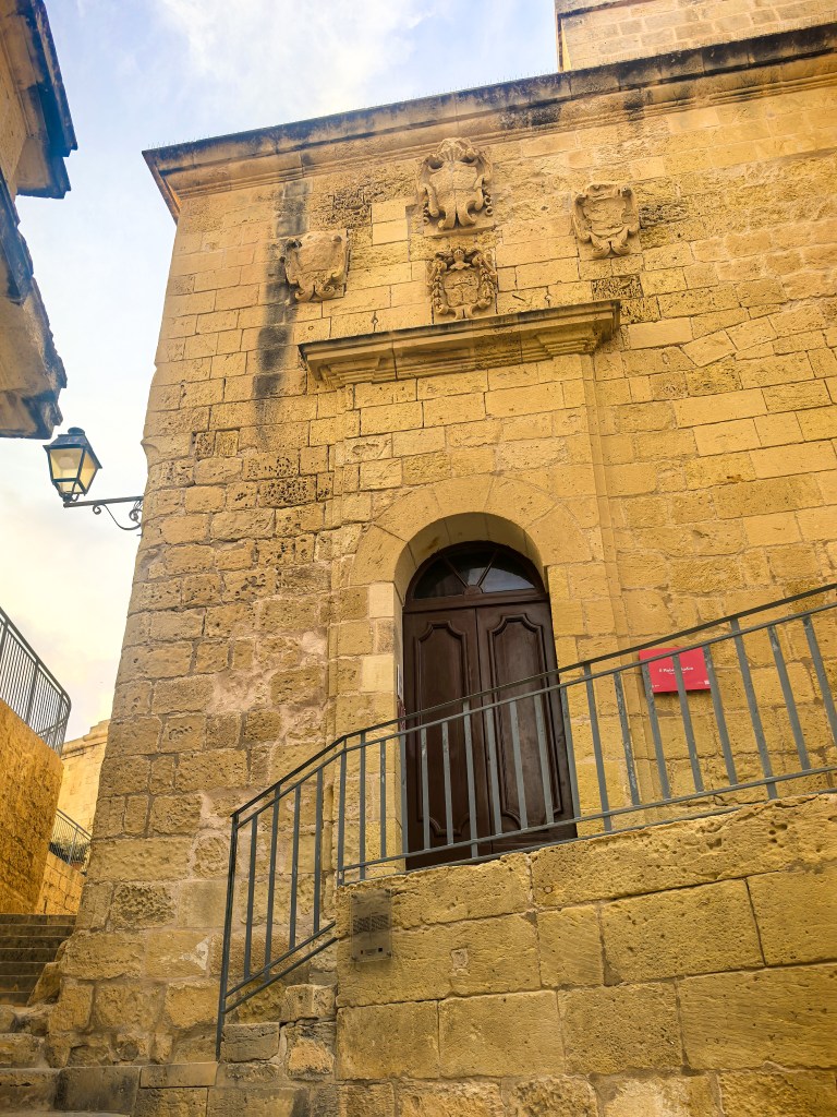 Porta de madeira escura na parede de pedra da antiga prisão da Cittadella, decorada com brasões