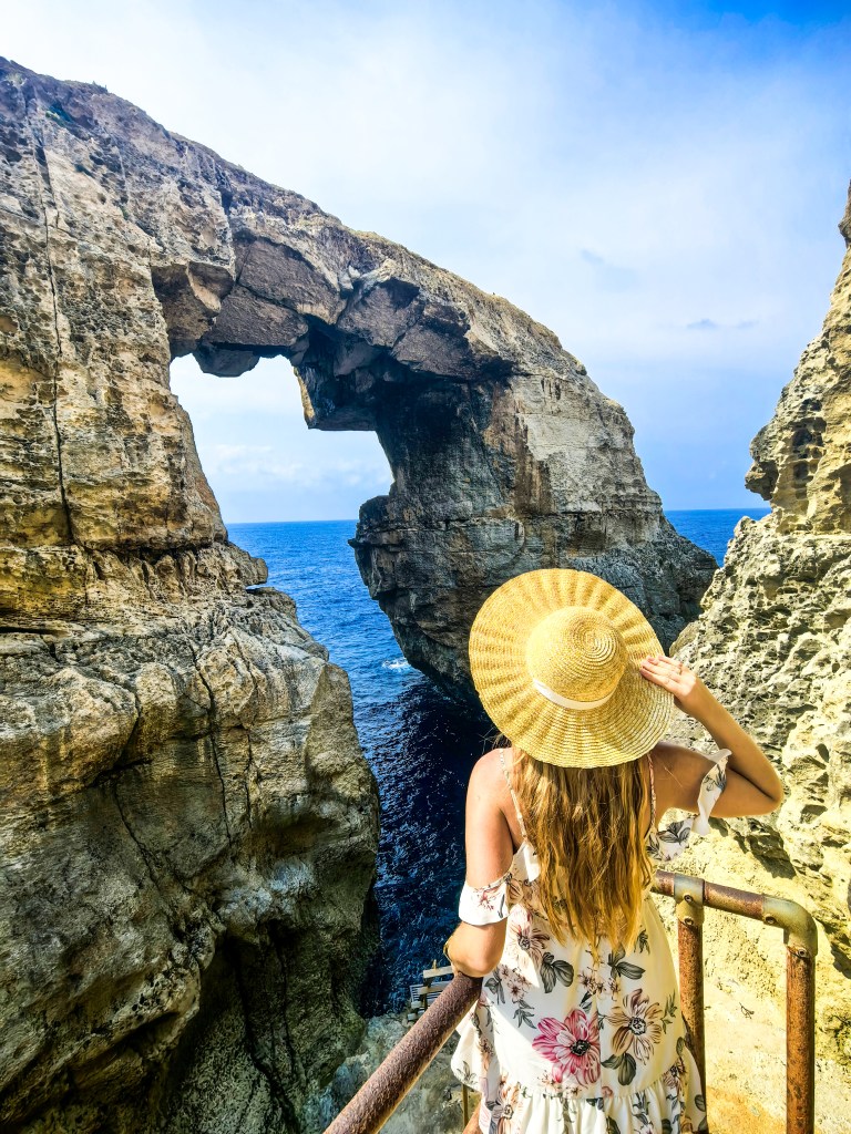 Mulher com chapéu admira o arco rochoso Wied il-Mielaħ sobre o mar azul em Gozo, Malta