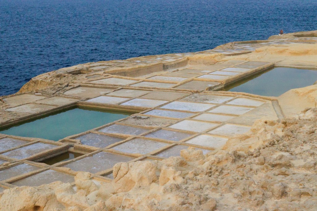 Salinas artesanais de Xwejni alinhadas na costa rochosa, com o mar azul ao fundo, Gozo, Malta