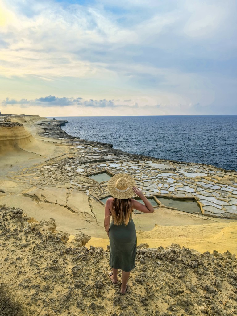 Mulher com chapéu olha para as tradicionais salinas de Xwejni, junto ao mar e falésias amarelas, Gozo, Malta