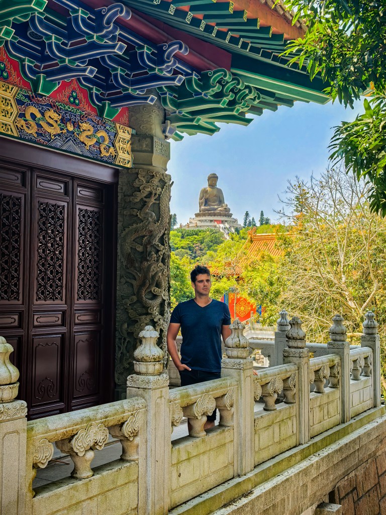 Man standing on Po Lin Monastery terrace with Tian Tan Buddha visible in the distance, Hong Kong.