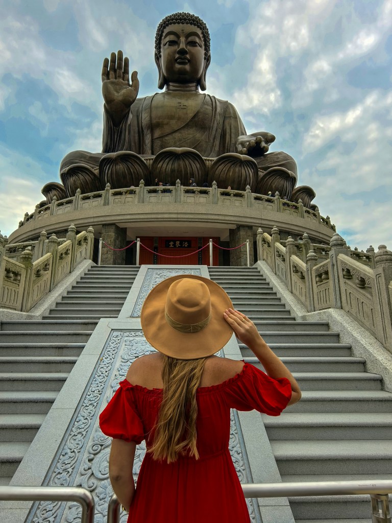 Visitor in a red dress and hat standing in front of the steps to Tian Tan Buddha, Hong Kong.