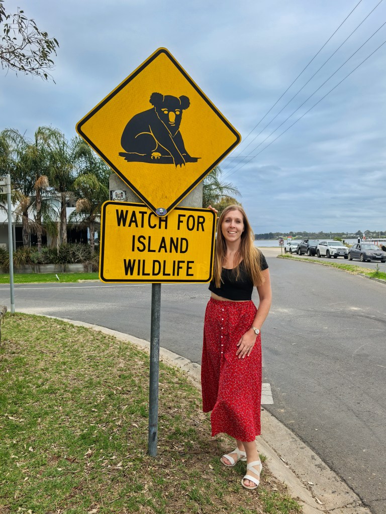 Female tourist standing next to a road sign warning about koalas on Raymond Island, Australia.