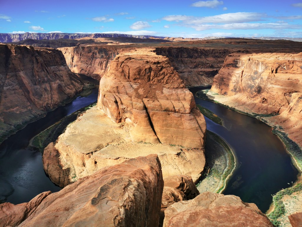 Klasyczny widok Horseshoe Bend w pełnym słońcu, z majestatycznym skalnym monolitem otoczonym zielonkawoniebieskimi wodami rzeki Kolorado.