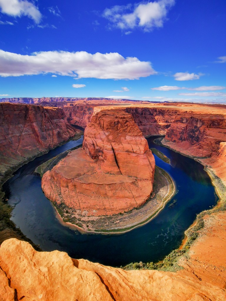 Widok na Horseshoe Bend, kanion w kształcie podkowy, z rzeką Kolorado przepływającą wokół czerwonych skał w Arizonie pod błękitnym niebem z chmurami.
