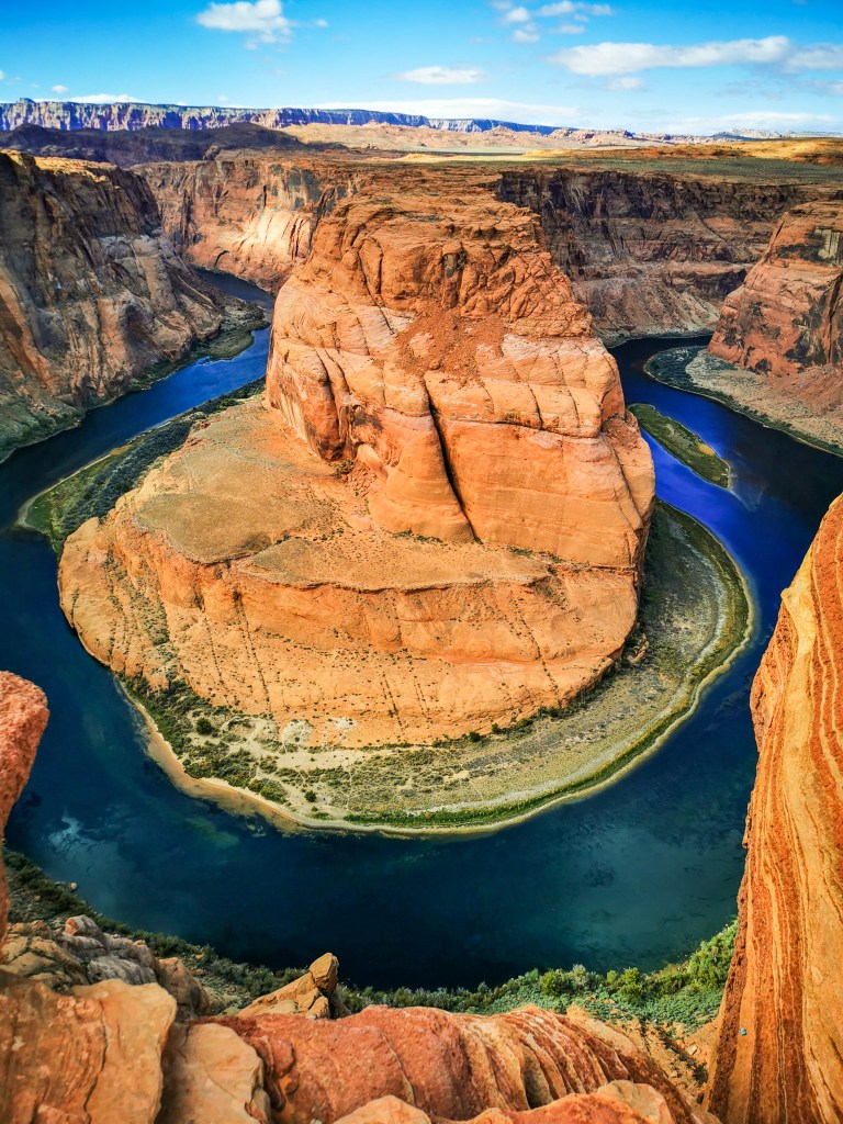 Pionowa panorama Horseshoe Bend ukazująca skalny monolit otoczony turkusową wodą rzeki Kolorado i strome ściany kanionu.