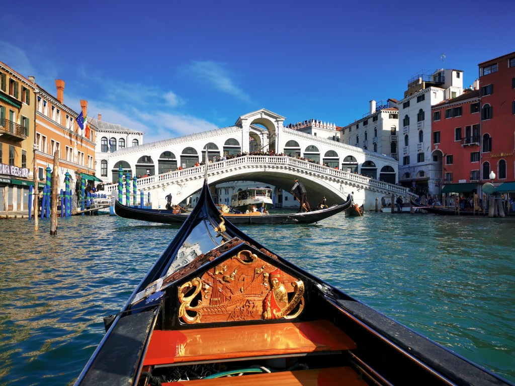 Widok na most Rialto w Wenecji z perspektywy gondoli płynącej po Canal Grande.
