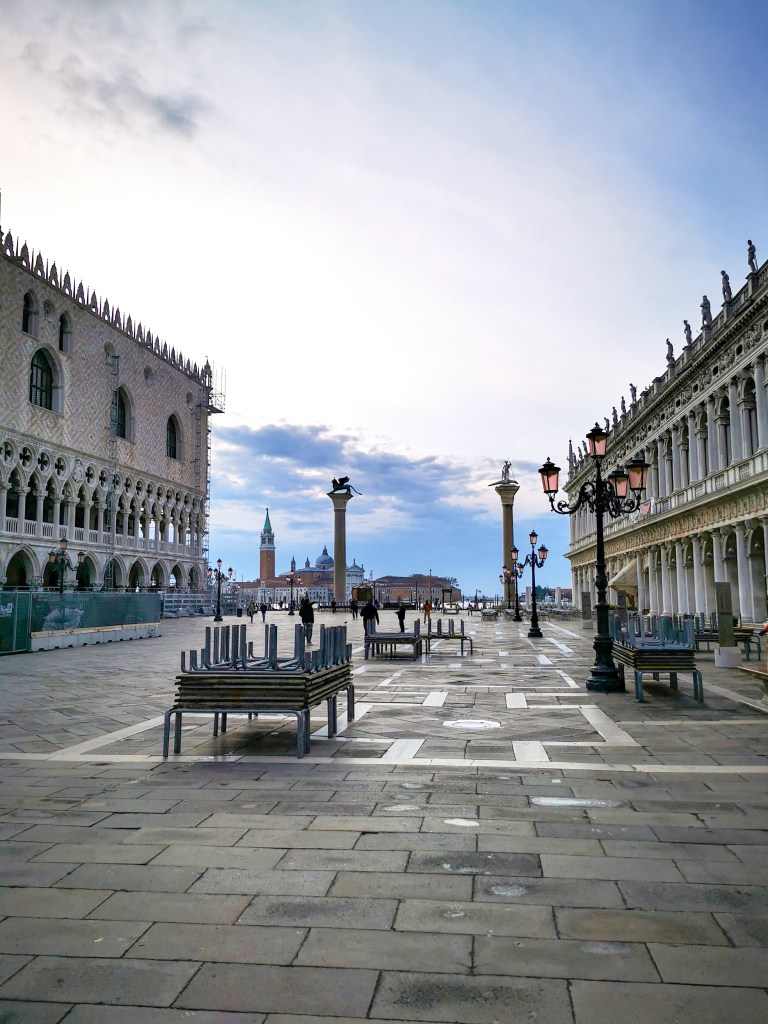 Pusty Plac św. Marka w Wenecji podczas acqua alta z rozstawionymi drewnianymi pomostami, arkadami Pałacu Dożów i kolumnami w tle.