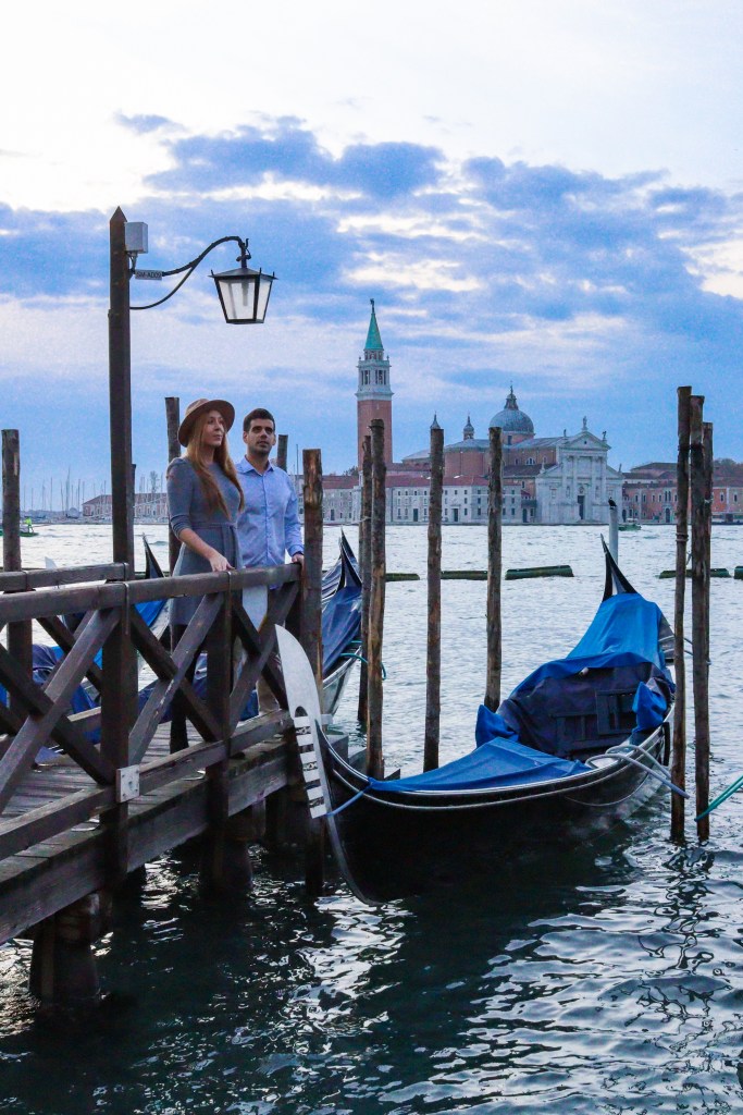 Para na pomoście Riva degli Schiavoni w Wenecji, z gondolami, kościołem San Giorgio Maggiore i dzwonnicą na tle laguny.