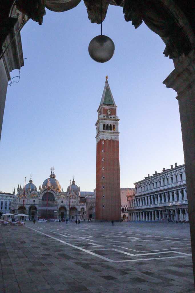 Veneza: Tudo o que deves saber antes da tua viagem Campanário de São Marcos enquadrado por um arco de pedra ao amanhecer na Praça de São Marcos