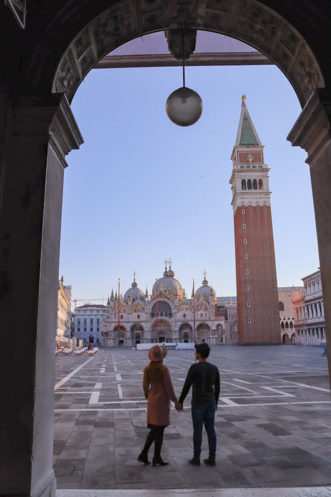 Veneza: Tudo o que deves saber antes da tua viagem Casal de mãos dadas na Praça de São Marcos com a basílica e o campanário em Veneza
