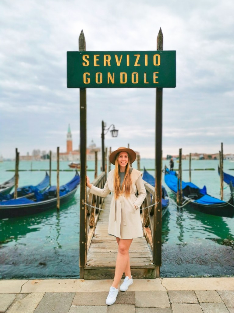 Veneza: Tudo o que deves saber antes da tua viagem Mulher de casaco bege no cais Servizio Gondole com gôndolas na lagoa de Veneza