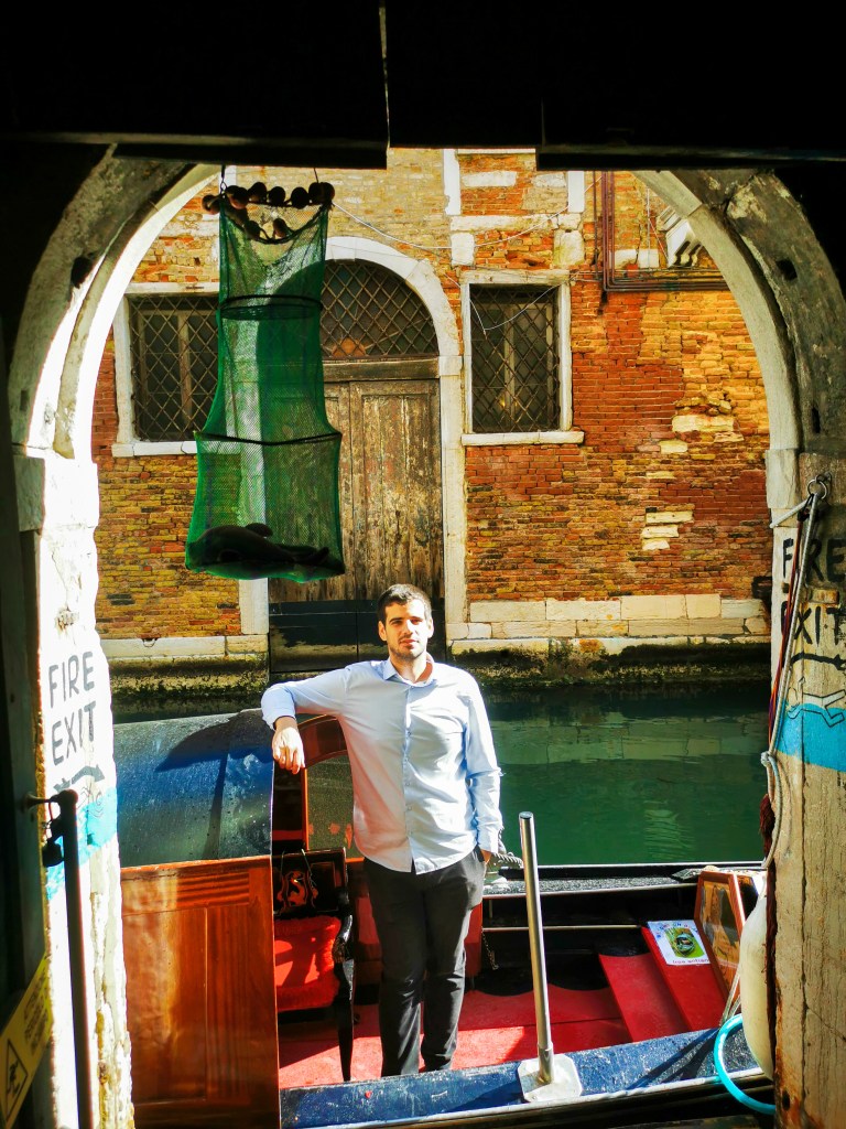 Venice: Everything You Should Know Before Your Trip Man standing in a gondola inside Libreria Acqua Alta bookshop on a Venice canal.