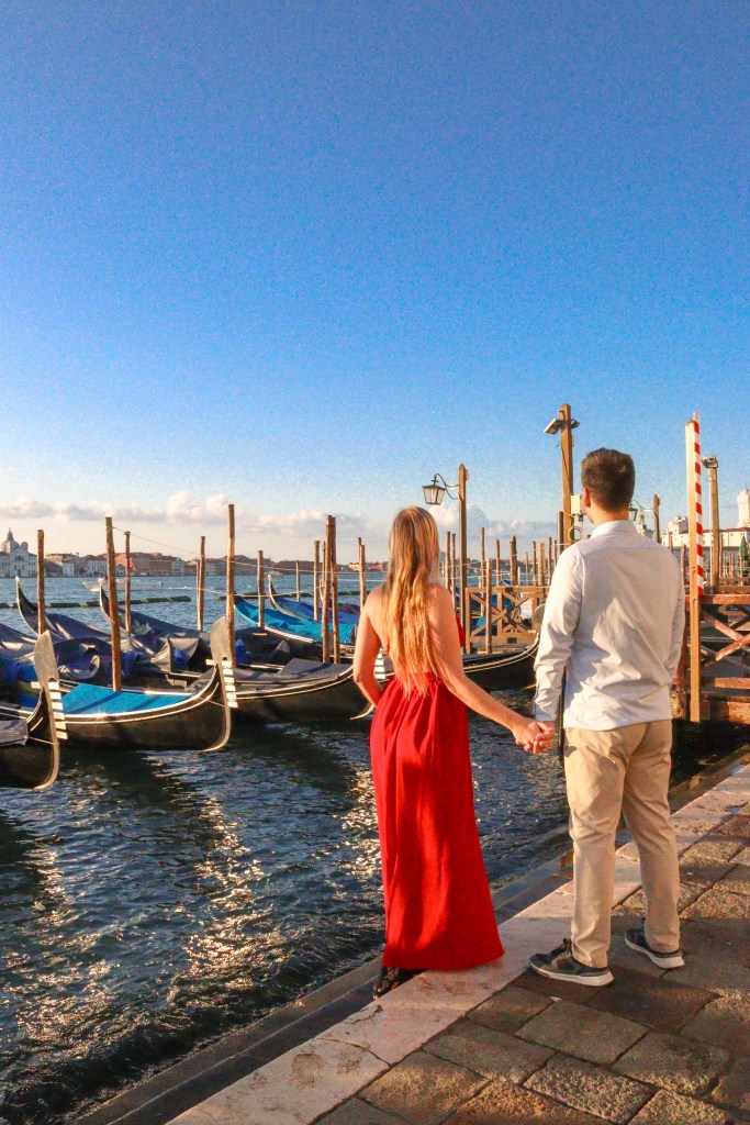 Para trzymająca się za ręce przy gondolach nad laguną w Wenecji na Riva degli Schiavoni podczas złotej godziny