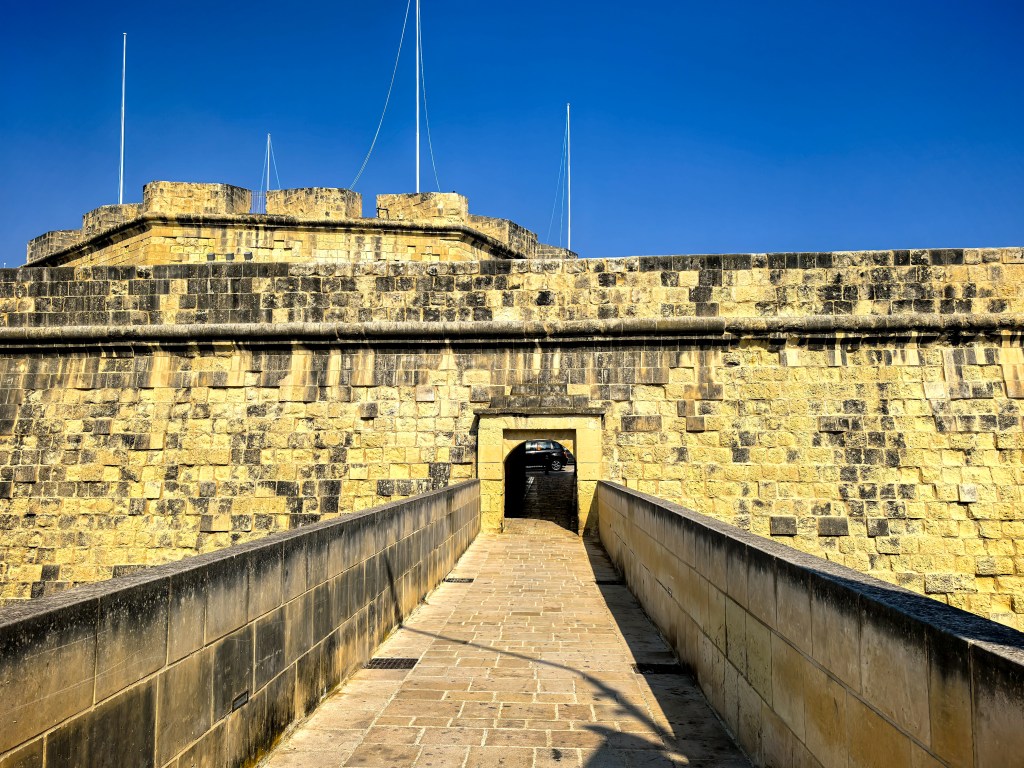 Kamienna brama Bastionu św. Jakuba w Birgu z masywnymi murami i mostkiem. Trzy Miasta.