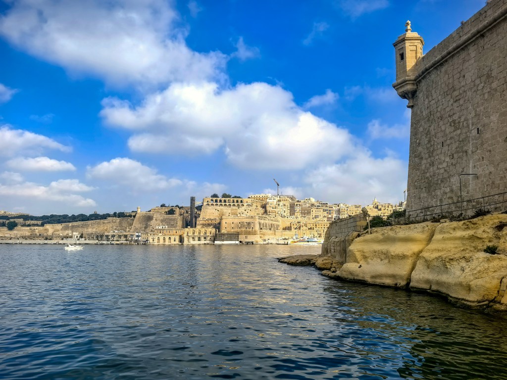 Panorama Valletty z nabrzeża w Birgu nad Grand Harbour, z fragmentem fortu św. Anioła i błękitnym morzem.