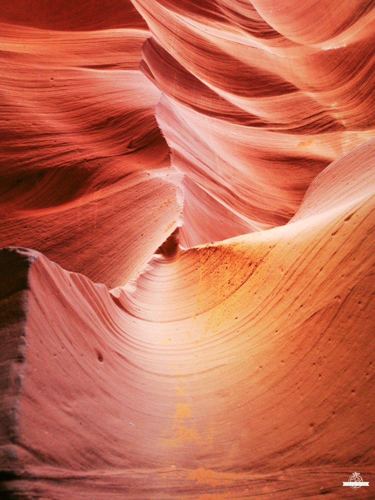 Paisagem impressionante do Lower Antelope Canyon, com formações rochosas curvas em tons de vermelho e laranja, iluminadas pela luz natural filtrada pelas fendas superiores.
