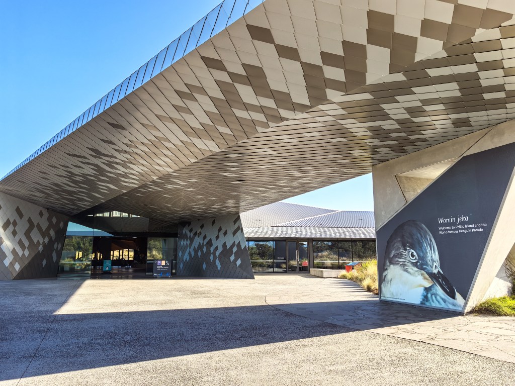 Modern building entrance with a large patterned roof canopy and a penguin welcome sign at Penguin Parade, Phillip Island, Australia.
