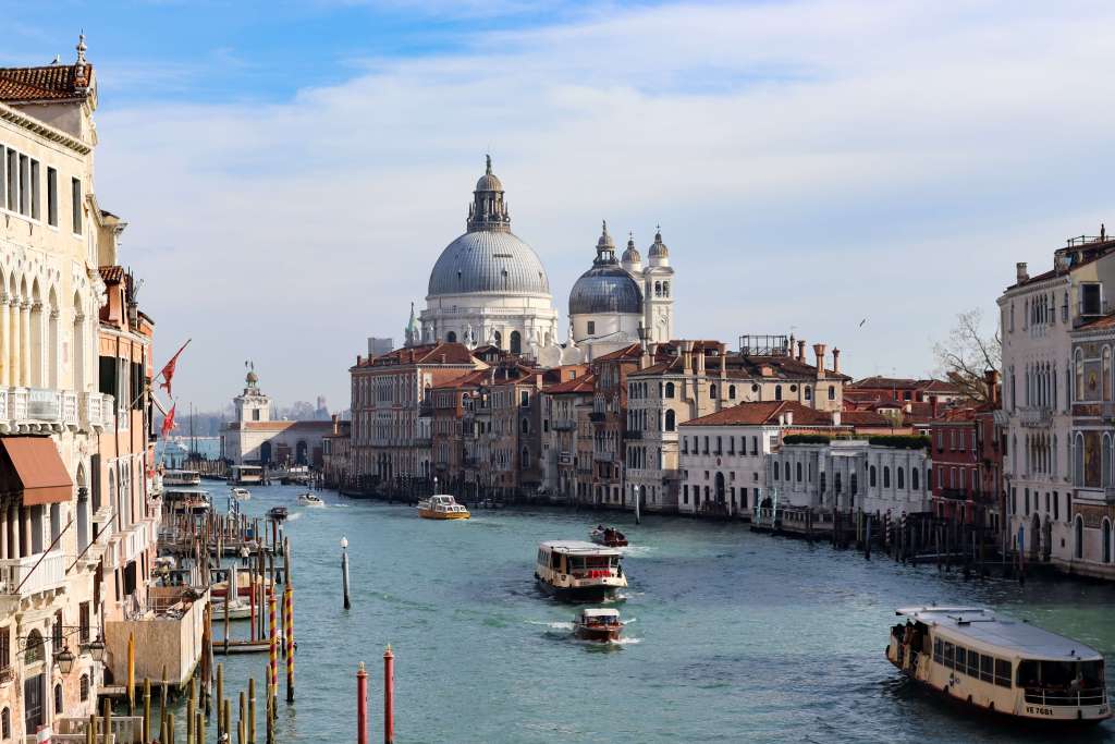 Wenecja – jak się poruszać po Mieście Dożów? Widok na Grand Canal w Wenecji z płynącymi vaporetto i bazyliką Santa Maria della Salute w tle w słoneczny dzień.
