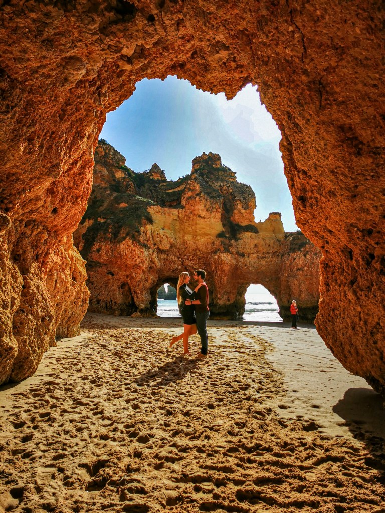 Our Top 7 Beaches in the Algarve Couple standing beneath natural rock arches at Praia dos Três Irmãos in Alvor