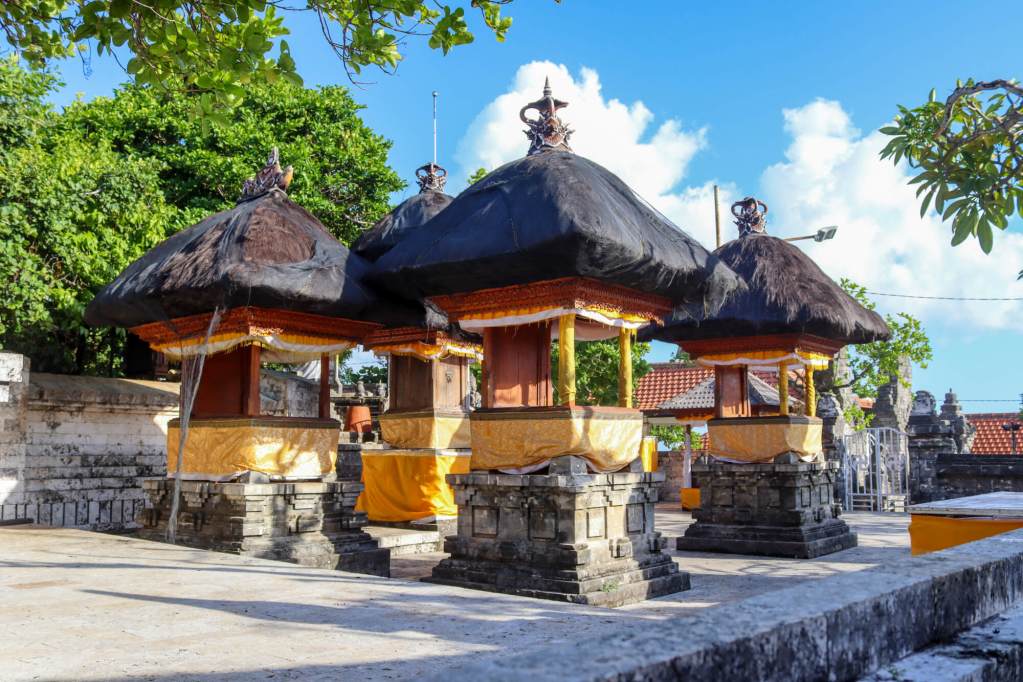 Świątynia Uluwatu, Bali – Kompletny przewodnik Tradycyjne balijskie kapliczki z czarnymi dachami ozdobione żółtym materiałem w Pura Luhur Uluwatu.