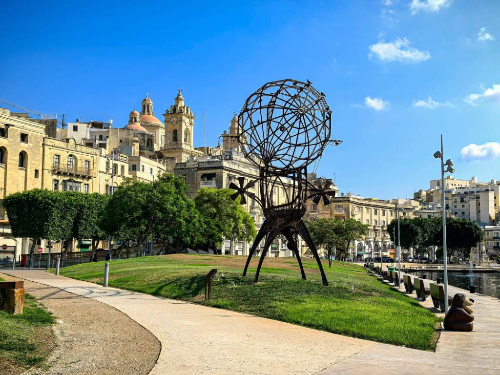 A Guide to Malta’s Three Cities: Discover Birgu, Isla and Bormla A large modern metal sculpture in a public park in Bormla (Cospicua) with the city skyline in the background.