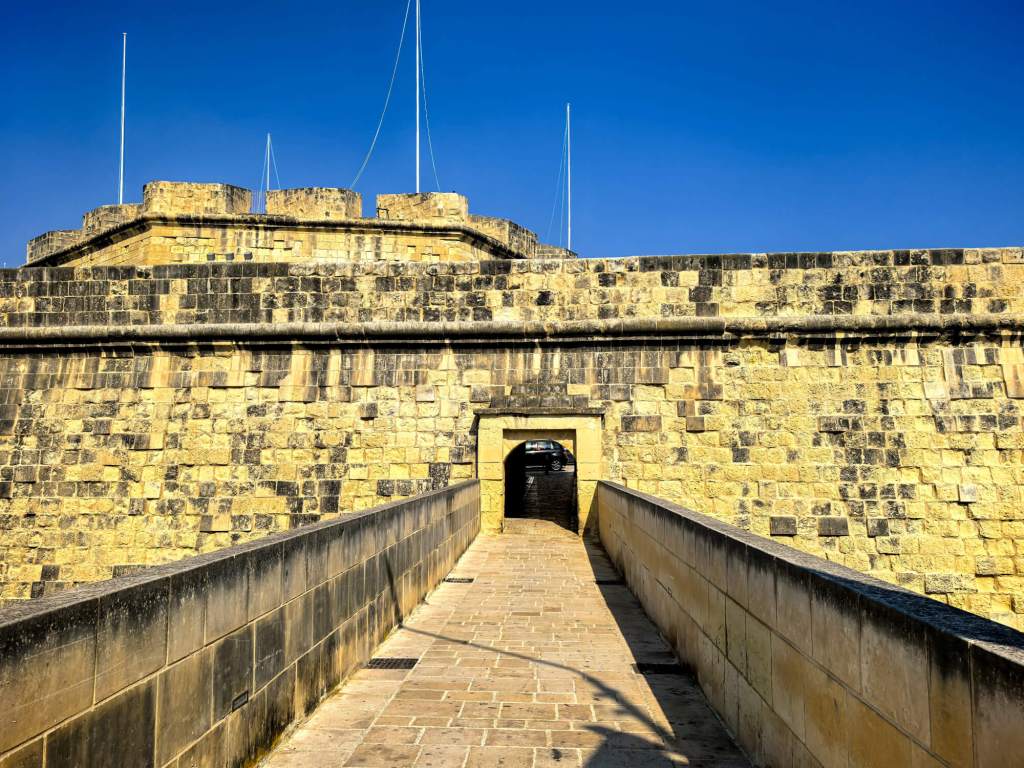 A Guide to Malta’s Three Cities: Discover Birgu, Isla and Bormla A long stone ramp leading into the massive limestone bastions of Fort St Angelo in Birgu under a clear blue sky.
