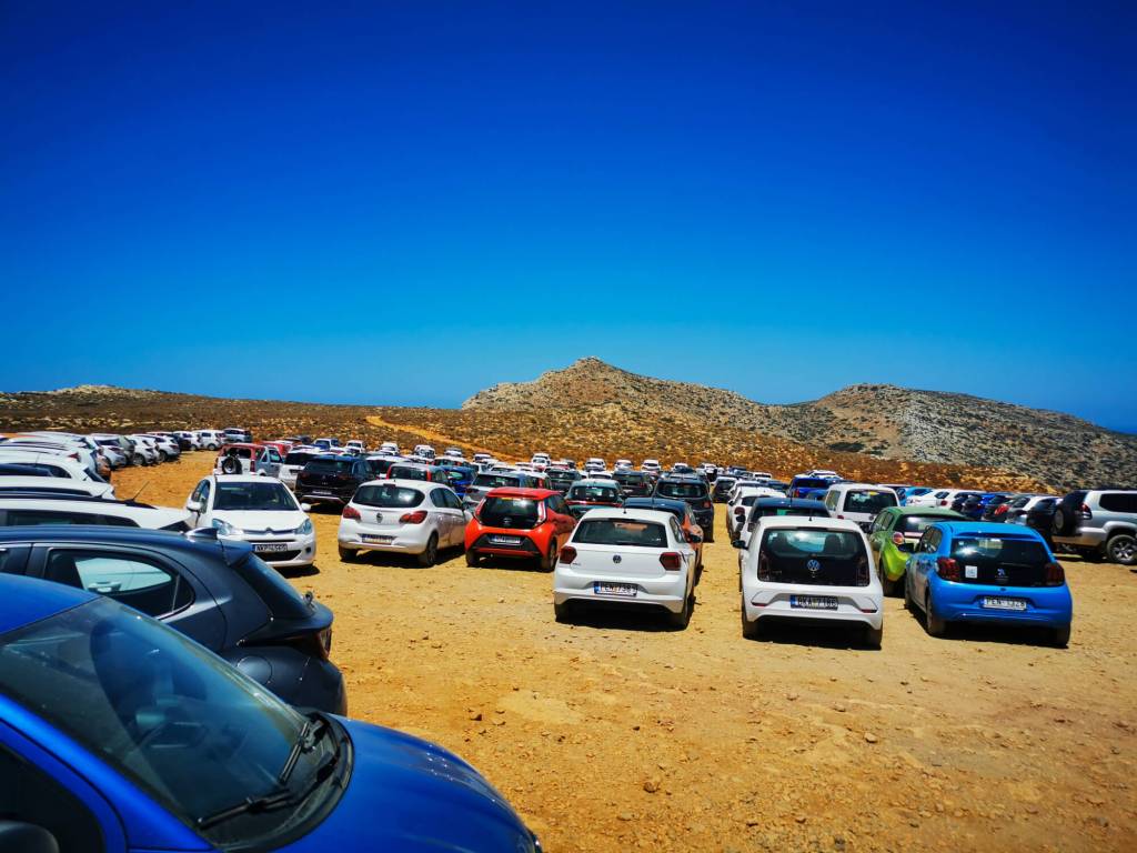 A busy dirt parking lot full of cars at the end of the road to Balos Lagoon in Crete.