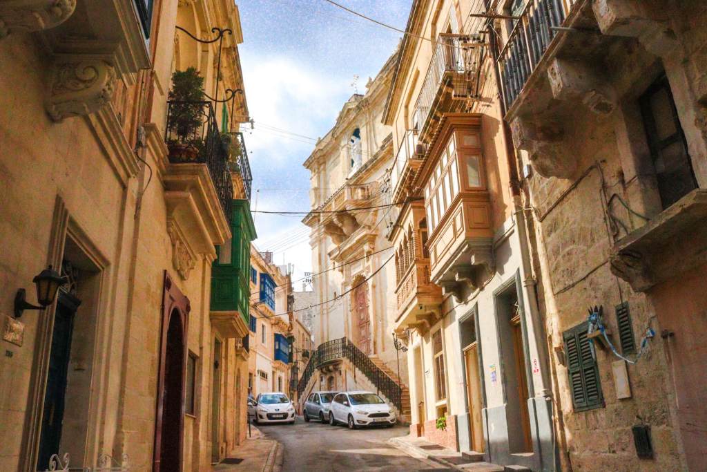 A Guide to Malta’s Three Cities: Discover Birgu, Isla and Bormla A narrow limestone street in Senglea (Isla) leading towards the facade of a historic Baroque church.