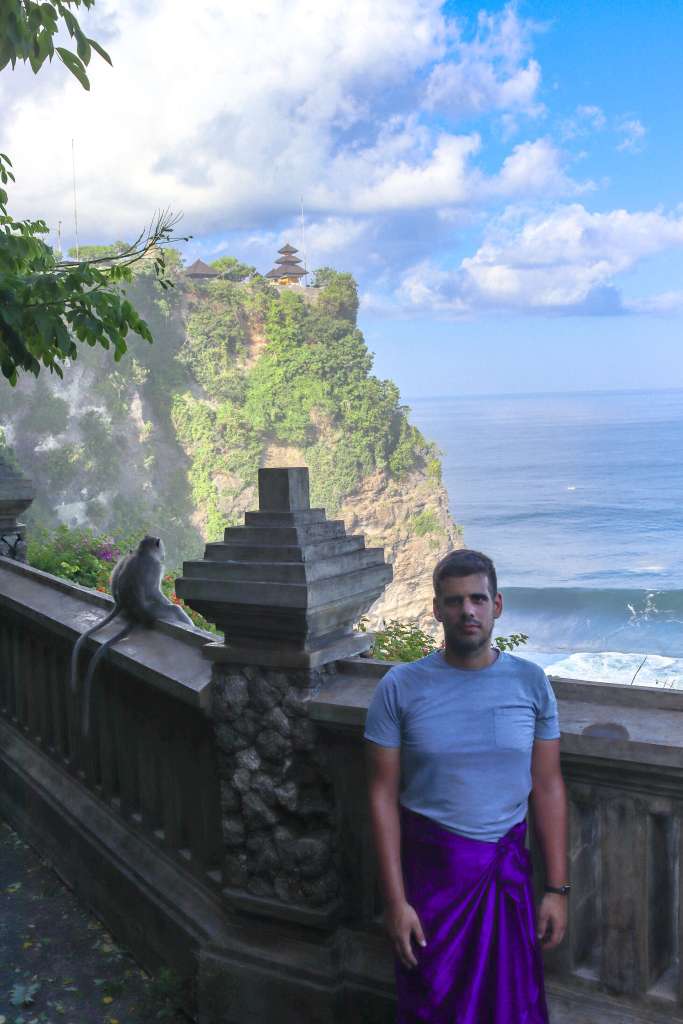 Świątynia Uluwatu, Bali – Kompletny przewodnik Turysta zwiedzający Pura Luhur Uluwatu, w tle na murku siedzi makak.