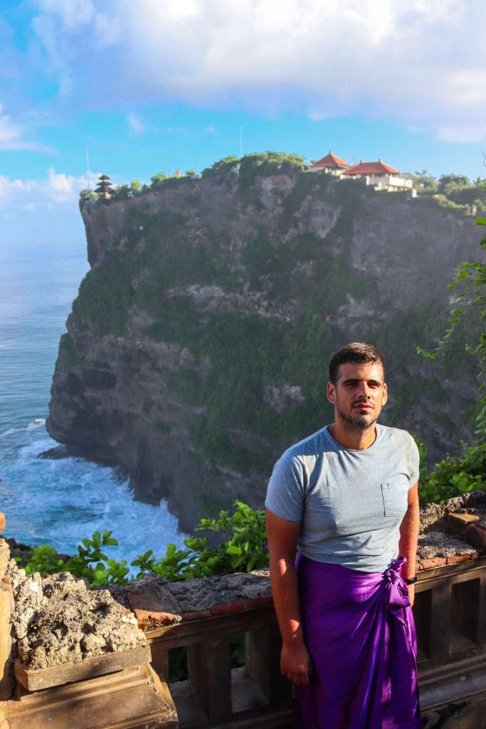Świątynia Uluwatu, Bali – Kompletny przewodnik Turysta w tradycyjnym fioletowym sarongu zwiedzający Pura Luhur Uluwatu.