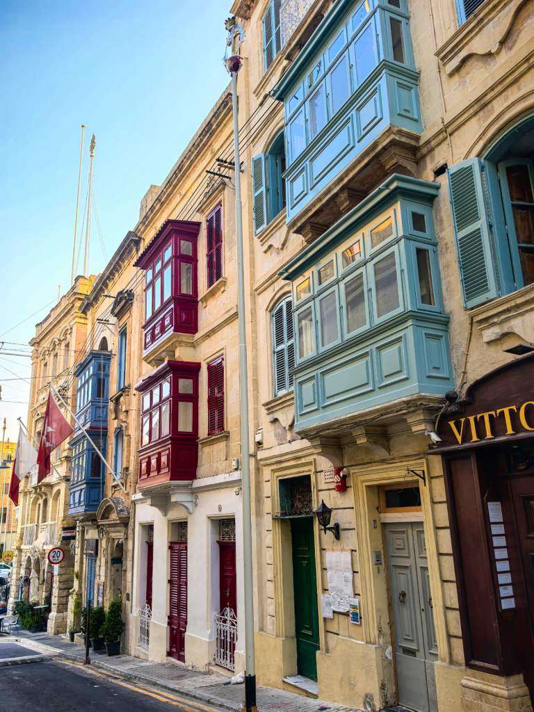 A Guide to Malta’s Three Cities: Discover Birgu, Isla and Bormla A narrow street in Birgu with multiple storeys of traditional red, blue, and green wooden balconies.