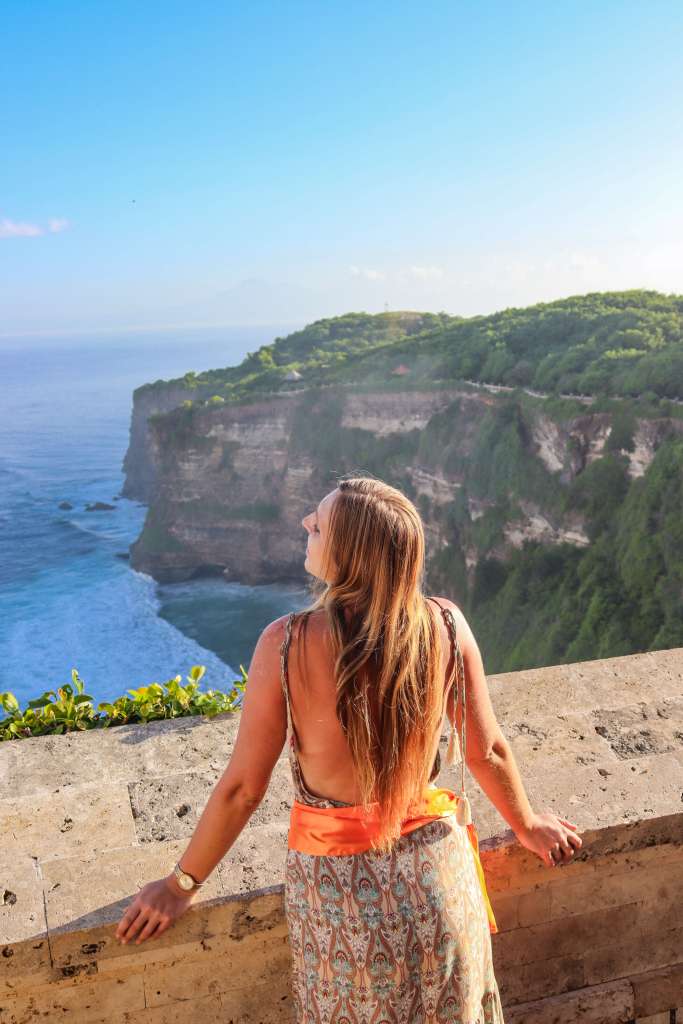 Świątynia Uluwatu, Bali – Kompletny przewodnik Kobieta z pomarańczową szarfą podziwia klify – Uluwatu Bali przewodnik i punkty widokowe.