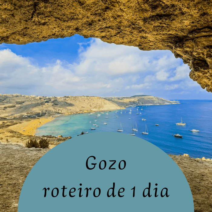 Panorama da Baía de Ramla vista do interior da Gruta Tal-Mixta, com mar azul, barcos ancorados e falésias douradas