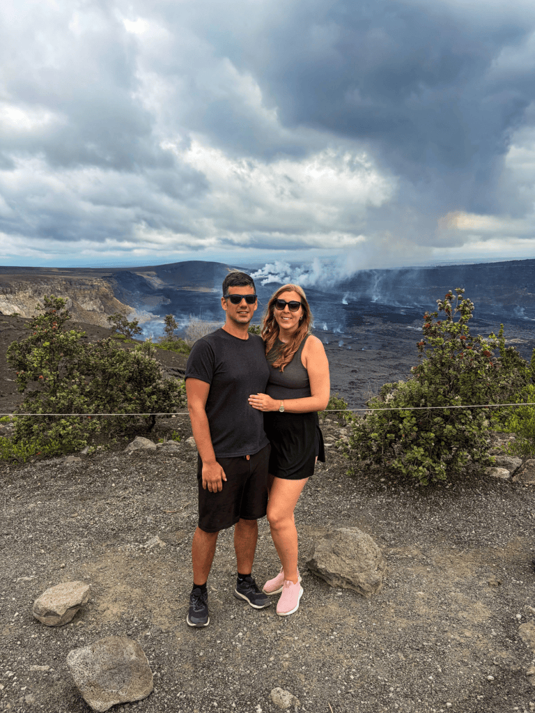 A couple at a viewpoint with a panoramic view of a volcanic crater and smouldering landscape in Hawaii.
