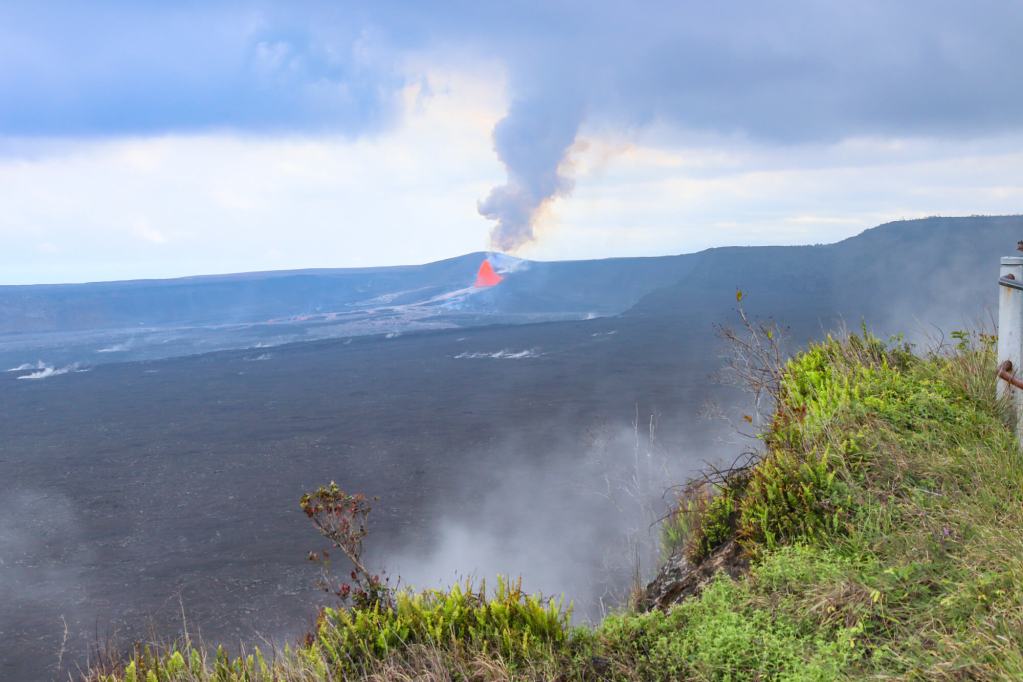 The eruption of Kīlauea in Hawaiʻi Volcanoes National Park on the Big Island, featuring a visible lava fountain and a plume of smoke.
