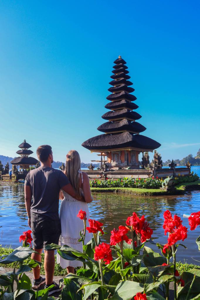 Para podziwiająca Pura Ulun Danu Bratan na Bali z czerwonymi kwiatami na pierwszym planie.