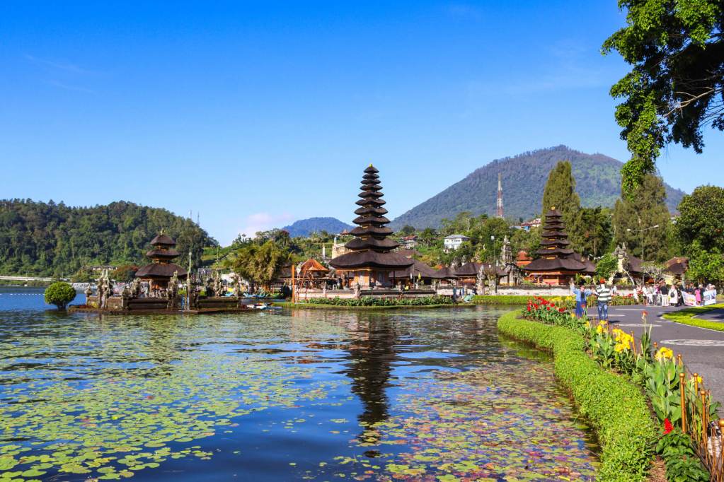 Panorama Pura Ulun Danu Bratan na Bali z jeziorem Bratan, liliami wodnymi i górami w tle.